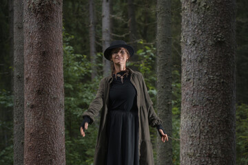 Naklejka premium A woman in a long coat and hat enjoys a peaceful moment in the forest
