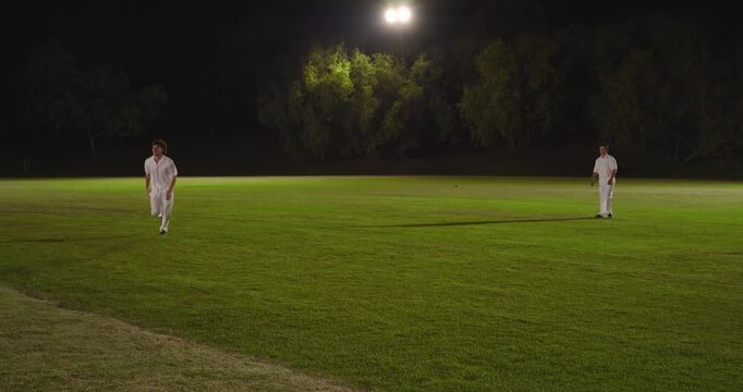 Tracking cricket ball under floodlight on grass male cricketer sprinting diving in gloves for catch