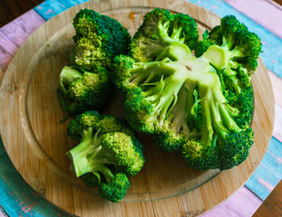 Fresh florets and a cut stem arranged on a round bamboo cutting board with water droplets and...