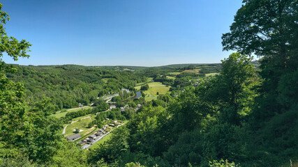High-angle panoramic view of a dense, lush green valley in the Belgian Ardennes with a small village.