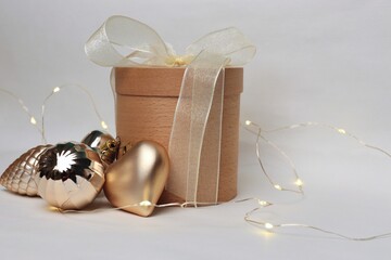 Round wooden gift box with white ribbon and golden Christmas ornaments on light background —...