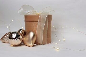 Round wooden gift box with white ribbon and golden Christmas ornaments on light background —...