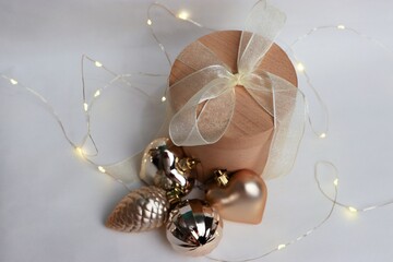 Round wooden gift box with white ribbon and golden Christmas ornaments on light background —...