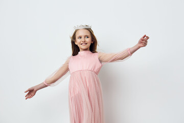 Elegant smiling girl in a pink dress with a crown, joyful expression, minimalist background...