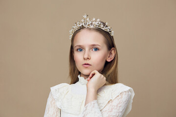 A young girl in a beautiful crown, wearing a delicate white dress, displaying an elegant expression...