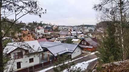 View of the city from the top of a grassy hill covered with birch and pine trees. There are various...