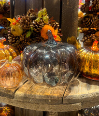Large silver glass pumpkin with smaller copper and gold pumpkins, set on rustic wood with autumn wreaths and pinecones in the background.