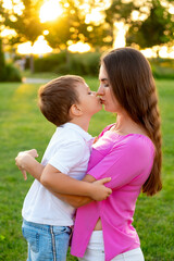 Fototapeta premium mother and child are walking, playing on a green lawn in the summer, having fun together, mother and son are hugging and kissing, laughing and smiling