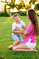 Fototapeta premium mother and child are walking, playing on a green lawn in the summer, having fun together, mother and son are hugging and kissing, laughing and smiling