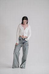 Pretty young fashion sensual woman posing on white wall background dressed in white top and jeans...