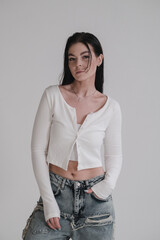 Pretty young fashion sensual woman posing on white wall background dressed in white top and jeans...