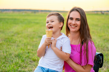 mother and child walking and eating ice cream in the summer on a green lawn, having fun together,...