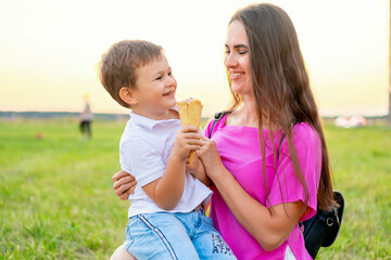 mother and child walking and eating ice cream in the summer on a green lawn, having fun together,...