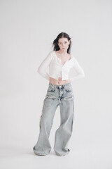 Pretty young fashion sensual woman posing on white wall background dressed in white top and jeans...