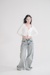 Pretty young fashion sensual woman posing on white wall background dressed in white top and jeans...