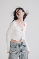 Pretty young fashion sensual woman posing on white wall background dressed in white top and jeans...