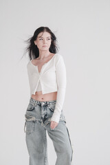 Pretty young fashion sensual woman posing on white wall background dressed in white top and jeans...