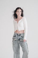 Pretty young fashion sensual woman posing on white wall background dressed in white top and jeans...