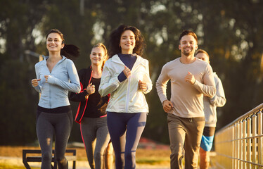 Group of active women and men runners jogging in park with cheerful expressions, leading healthy...