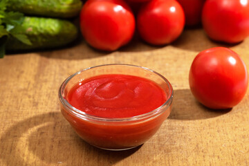 Bowl of ketchup or tomato sauce and fresh tomatoes on wood table