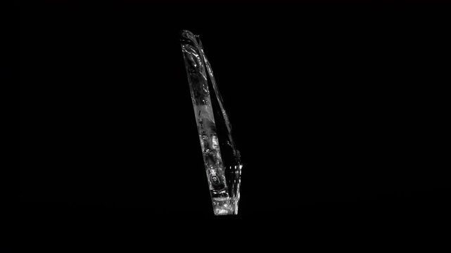 A thin, elongated shard of broken glass rotates gracefully against a black backdrop, catching light in its edges.