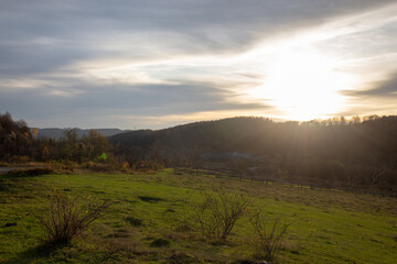 The golden light of sunset paints a peaceful countryside scene with rolling hills and a green field.