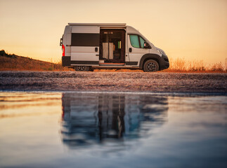 view to white camper van on the alone beach in evening time with reflections in calm water and...