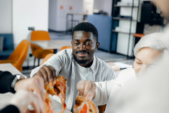 Diverse group of colleagues sharing pizza during casual office lunch break, promoting team bonding and relaxed work environment with focus on camaraderie and cultural inclusivity. - Powered by Adobe