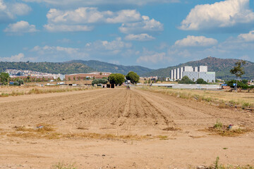 Perspective of a barren plowed field overlooking a residential area and mountains, showing the...