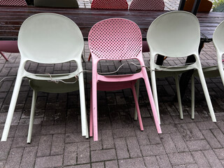 Close-up view of stacked pastel green and pink plastic chairs leaning against a wooden table on wet...