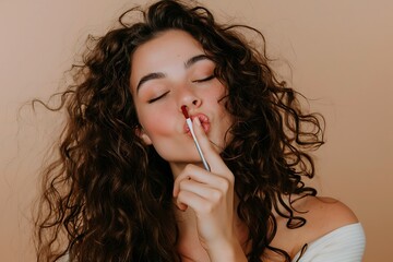 Curly haired woman smiling with closed eyes, Holding lipstick with joyful expression, Studio beauty portrait on beige background, Soft feminine makeup style