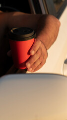 A close-up of a hand holding a red coffee cup. The background is blurred, providing ample copy...