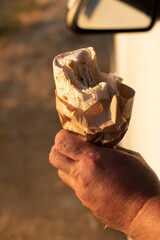 A hand holds an fast food. The background is blurred, suggesting a warm day. Add copy space,...