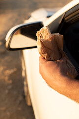 A hand holding a wrapped sandwich leans out of a car window. The scene captures a casual outdoor...