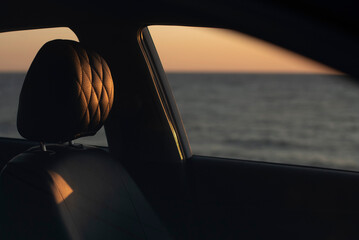 A car interior with a focus on the headrest and window, overlooking a serene ocean at sunset. The...