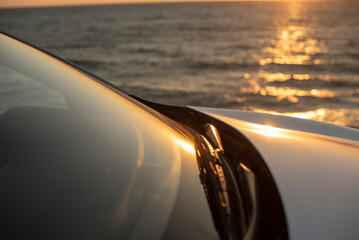 Obraz premium A close-up of a car's windshield with sunlight reflecting off the water in the background. The scene conveys a sense of freedom and adventure by the sea.