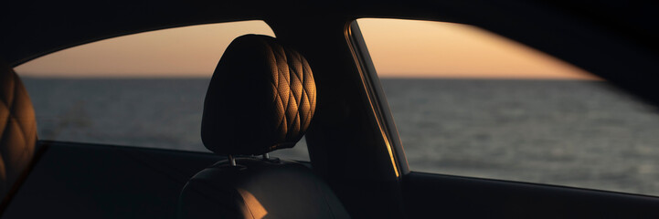Interior view of a car with a leather seat, overlooking a sunset by the ocean. The scene captures a...