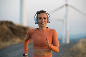 Young sportswoman running outside listening to music with headphones near wind turbines