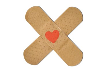 A pair of adhesive bandages arranged in a cross shape with a red heart at the center, isolated on white background.