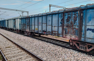 Freight train with blue open wagons parked on railway track during daylight, captured from side...