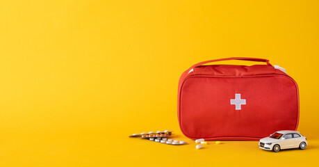 Red medical first aid bag placed near medicine tablets and a toy car showcasing emergency...