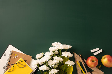 Teacher's desk decorated with flowers, apples, notebooks, and stationery on a green background...