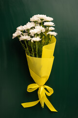 White vertical flowers arranged in a bright yellow paper bouquet with a ribbon tied neatly, evokes...