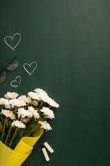 White vertical daisies in a yellow wrapping placed on a green chalkboard with chalk pieces