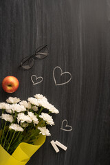 Apple, glasses, bouquet, and chalk on a vertical blackboard with hearts symbolizing teacher's day