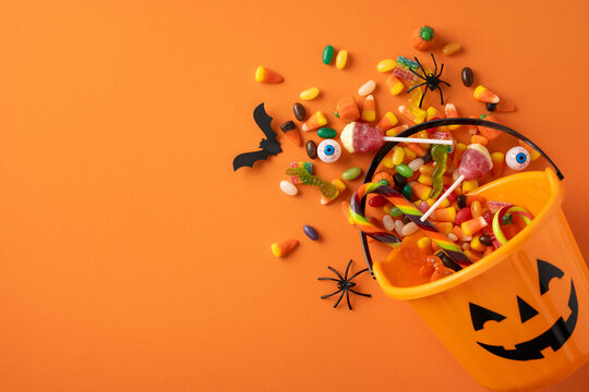 An orange Halloween bucket spills vibrant candies and decorations on a green backdrop