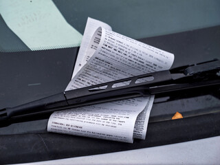 Closeup view of printed parking fine notice placed under windshield wiper on a car in Soller...