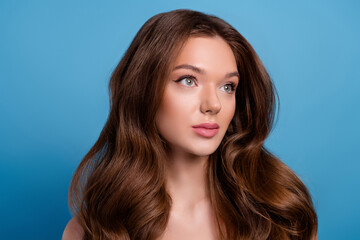 Portrait of a young woman with long wavy brown hair and glamorous makeup on a vibrant blue...