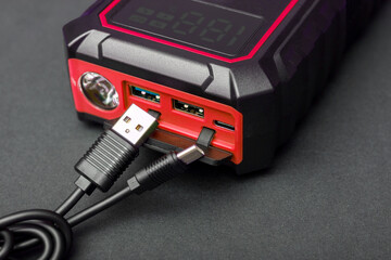 Charging portable jump starter via USB port. Multifunctional booster unit with flashlight and...