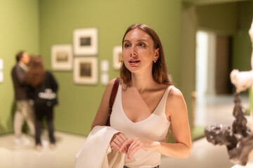 Young woman at an exhibition of photographs in a gallery. European woman in the hall of modern art looks with interest at photographs and paintings